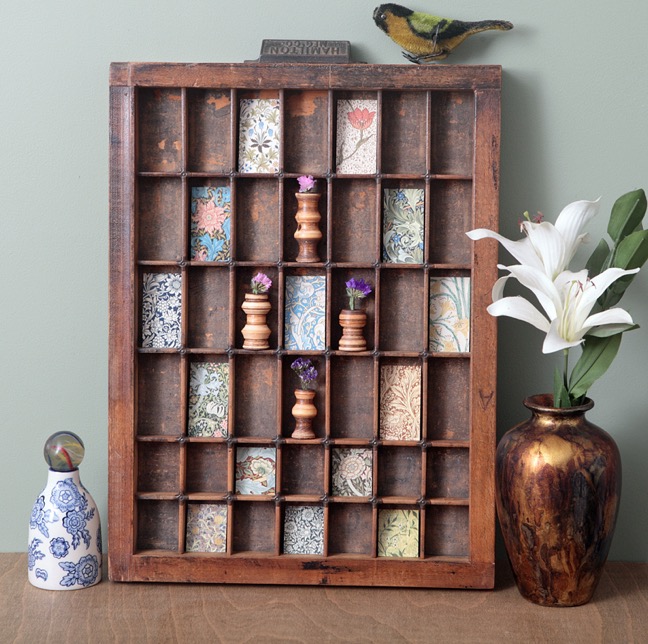 Little quirky display of hand turned wooden vases and decorative prints in vintage antique printers tray type case