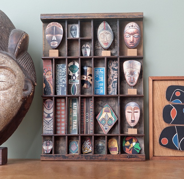 Handmade African mask ornaments and other African themed original artworks and photography displayed in an old antique letterpress printers tray type case drawer.