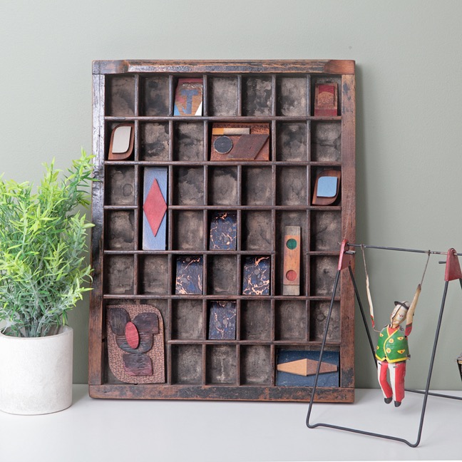 Small assemblage artwork using old vintage board and old solid wood shapes – some with colour. Displayed in an Antique letterpress printers tray with great time worn patination.