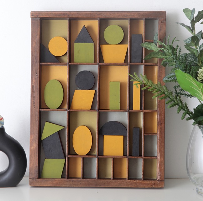 Assemblage artwork of geometric coloured wooden blocks in an vintage letterpress printers type case drawer tray 